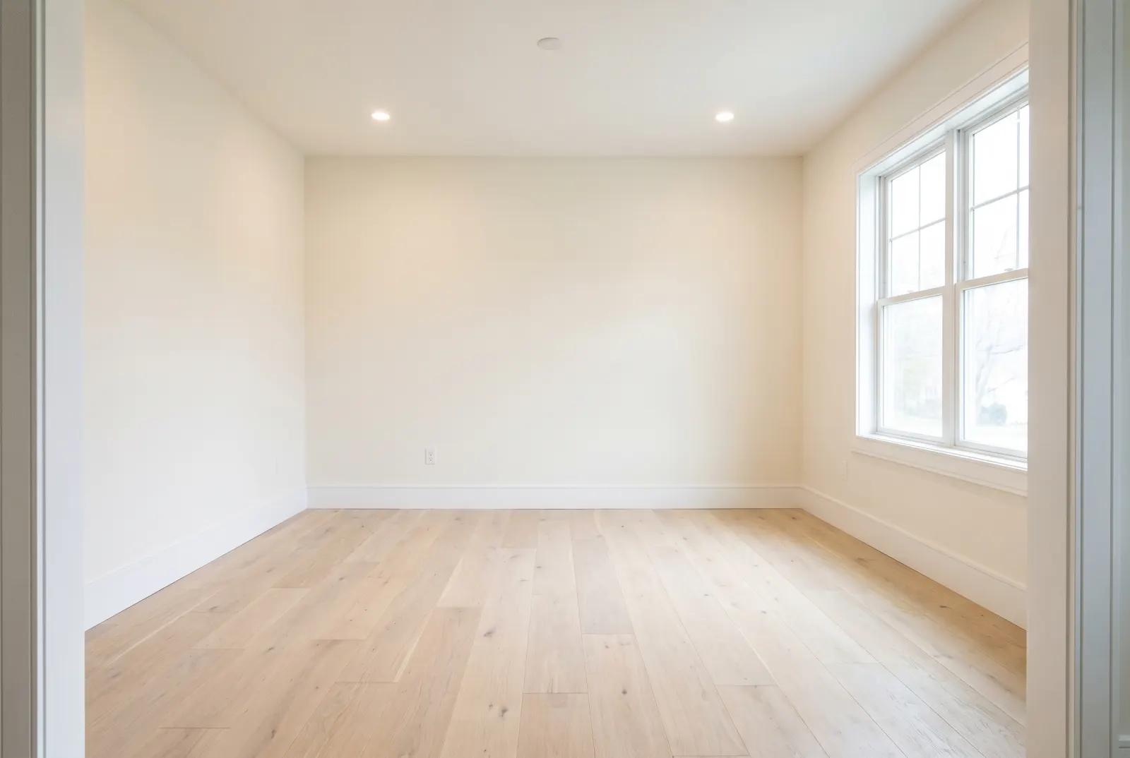 Empty living room with light oak floors and a large window