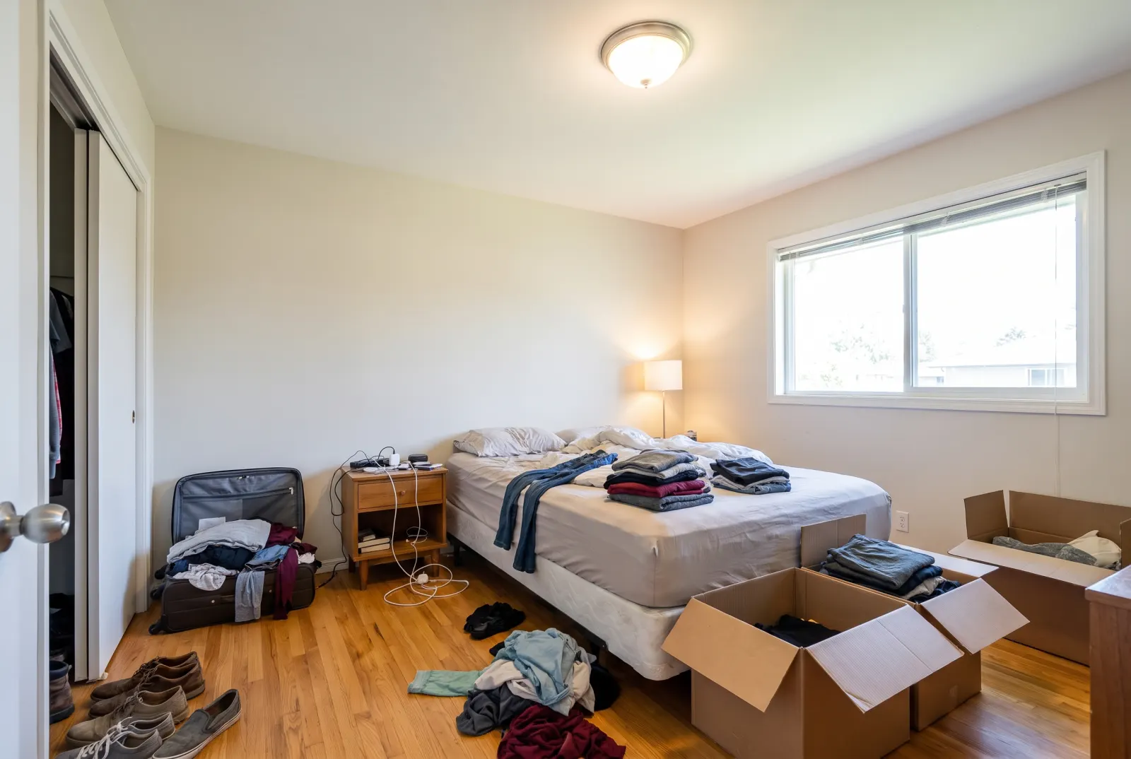 Cluttered bedroom with clothes and moving boxes
